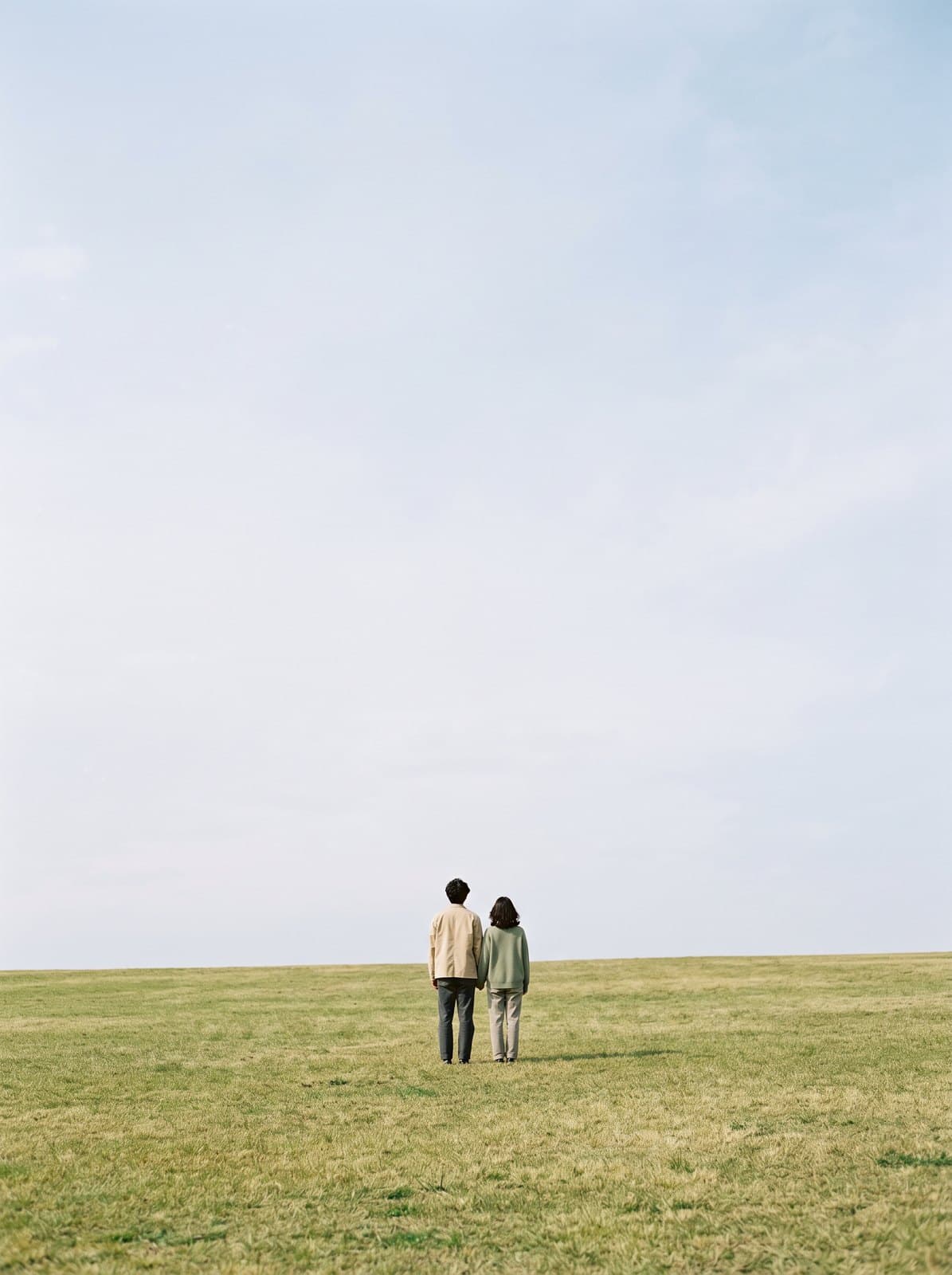 A couple on a lawn under a wide bright sky