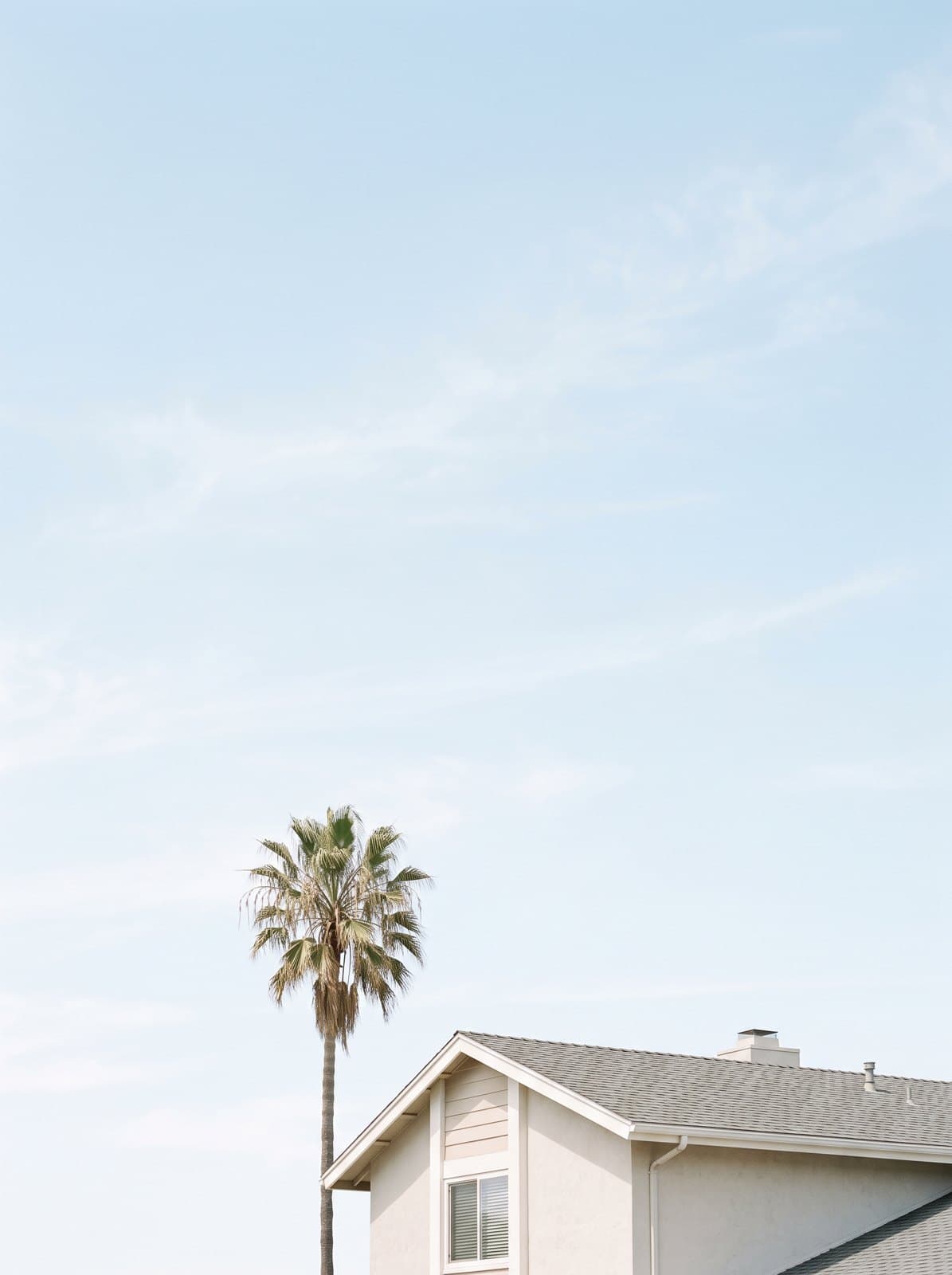The corner of a suburban home with a palm tree against the sky